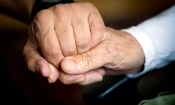 Възрастен мъж държи ръката на своя болногледач в стаята си в Берлин. (Odd Andersen/ Getty Images)