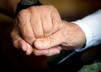 Възрастен мъж държи ръката на своя болногледач в стаята си в Берлин. (Odd Andersen/ Getty Images)
