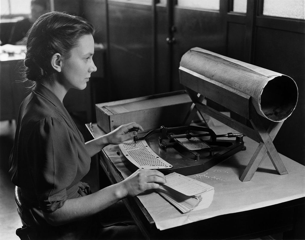 In 1940, a woman uses a punching machine to punch corresponding holes in a 1940 US Census card. The use of punch cards was one of the earliest stages of computerization; for their size, the cards could store more information than longhand records. (Public Domain)