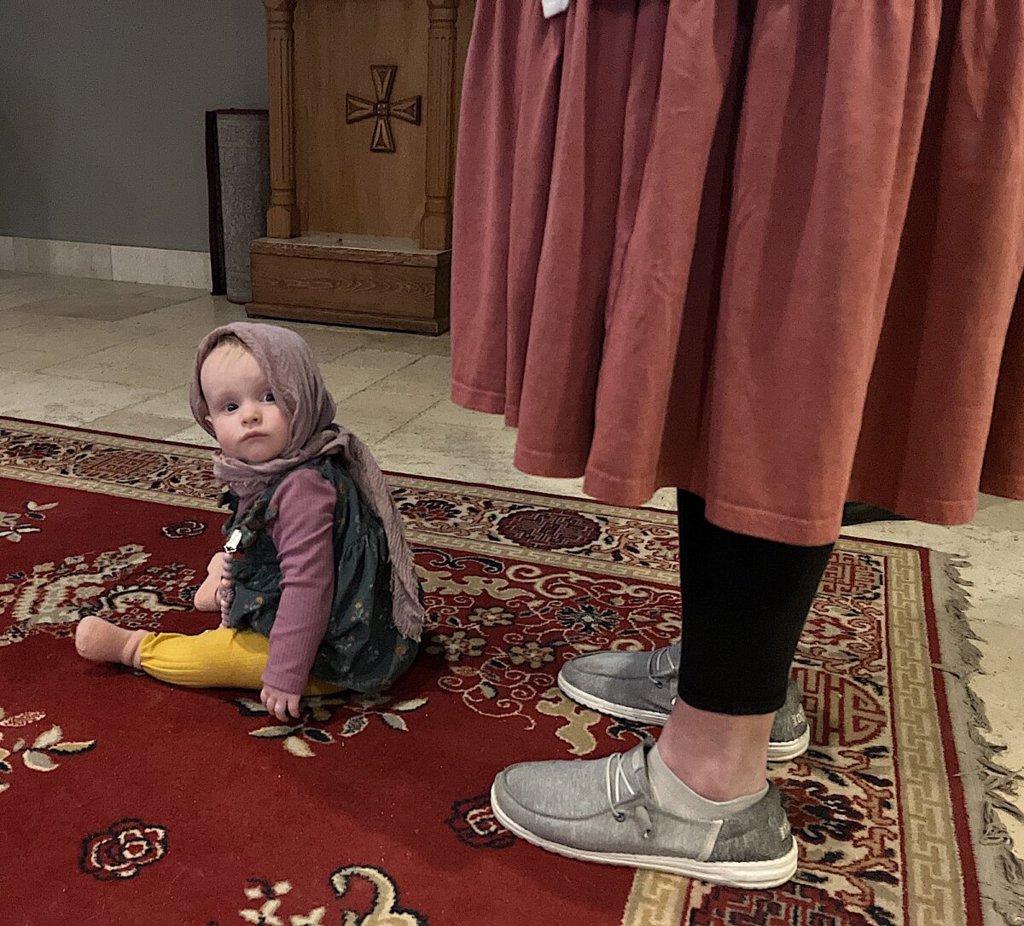 Войната в Украйна задълбочи разкола в Православната църква в САЩ 7 Малко момиченце в традиционно руско облекло седи в краката на майка си по време на служба в православната църква „Свети Архангели