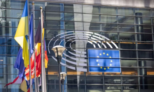 Знамена пред стъклената фасада на Европейския парламент с логото на парламента и флага на ЕС